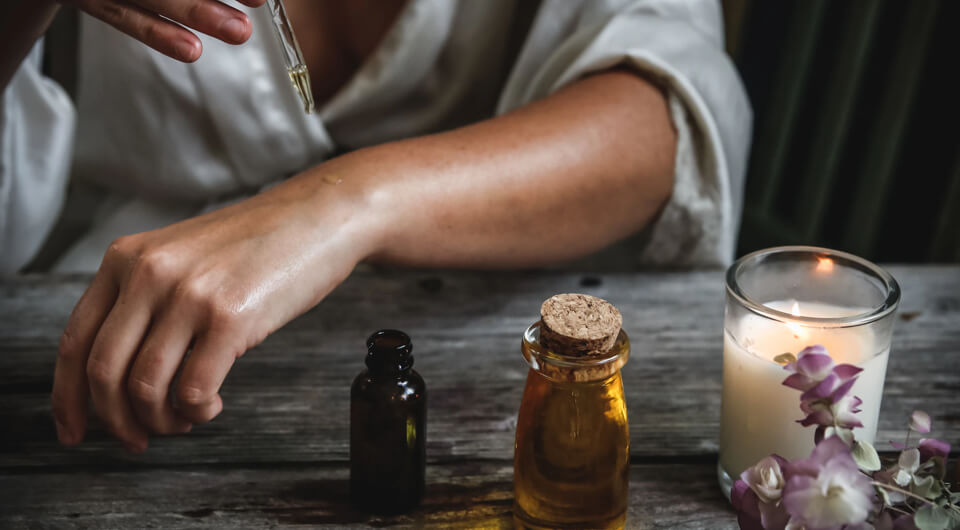 Frauenunterarm mit Öl; Kerze, Lavendel und Öl auf Tisch